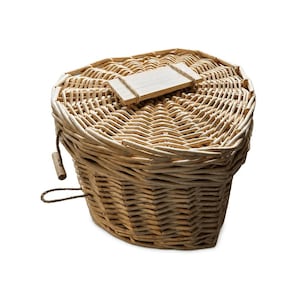 May include: A heart-shaped woven wicker basket with a lid. The basket features a light tan natural finish and a small rectangular wooden tag attached to the top of the lid with a thin piece of twine. A small wooden toggle is attached to the side.