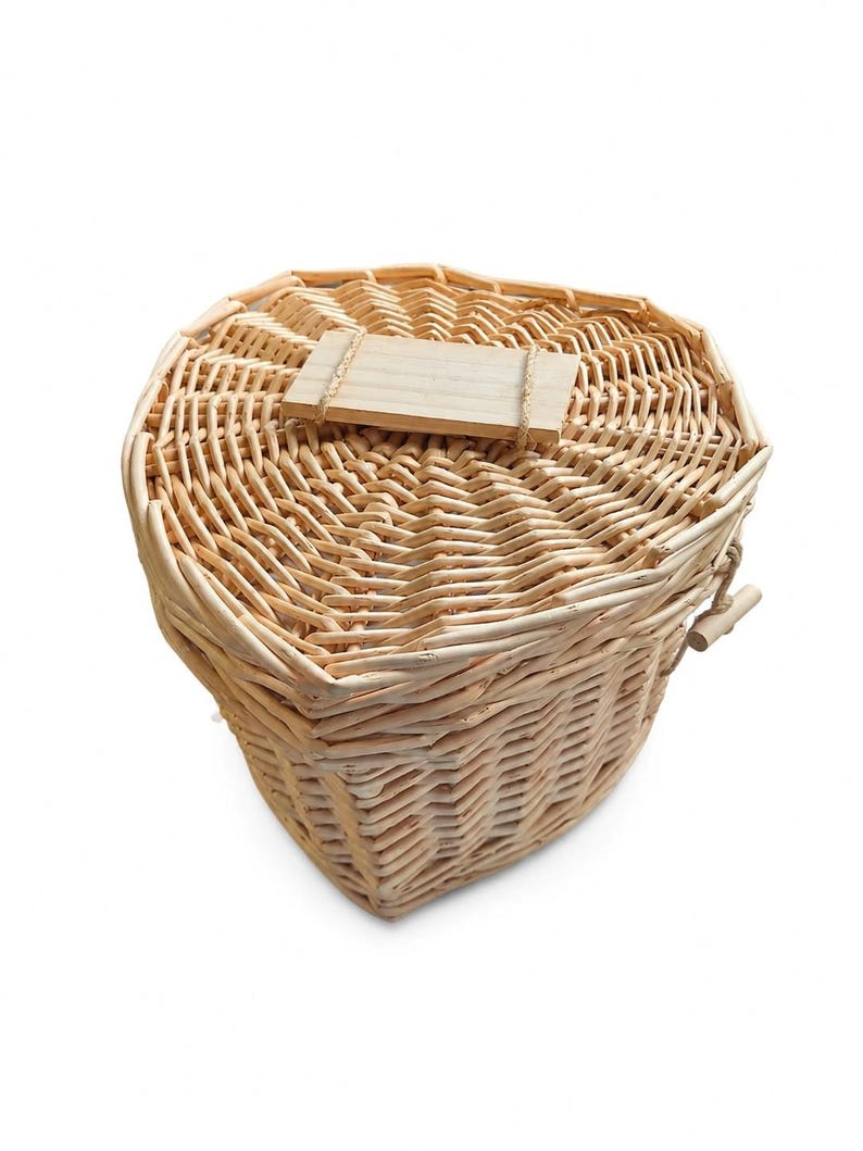 May include: A heart-shaped woven wicker basket with a matching lid. The basket features a light tan natural finish and a rectangular wooden plaque attached to the center of the lid with thin twine. The weave is tight and consistent throughout.