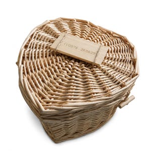 May include: A heart-shaped wicker basket with a light tan natural finish. A rectangular wooden plaque is attached to the lid with thin twine, featuring the engraved text 11/03/78 - 29/06/25. The basket has a woven texture and a lid.