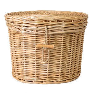 May include: A round, light brown woven wicker basket with a matching lid. The basket features a vertical weave pattern and a central closure mechanism consisting of a looped jute cord secured by a small, horizontal wooden toggle fastener.