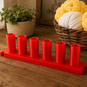 May include: A bright red plastic organizer stand featuring six vertical cylindrical holders arranged in a single row on a rectangular base. The stand has a smooth, solid finish and a small notch on the left side of the base for mounting or attachment.