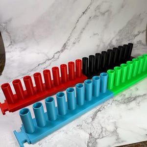 May include: Four modular storage racks in red, black, green, and blue, each featuring a single row of eight vertical cylindrical holders. The racks are designed with interlocking tabs on the ends to connect multiple units together in a line.