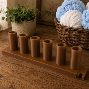 May include: A brown plastic organizer stand featuring six vertical cylindrical holders arranged in a single row on a rectangular base, with a small notched cutout on the right side of the base for additional storage or cable management.