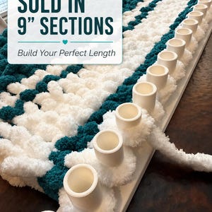 May include: A close-up of a chunky knit blanket in white and teal. The blanket is being constructed on a white loom with cylindrical pegs. Text on the image reads "SOLD IN 9" SECTIONS" and "Build Your Perfect Length."