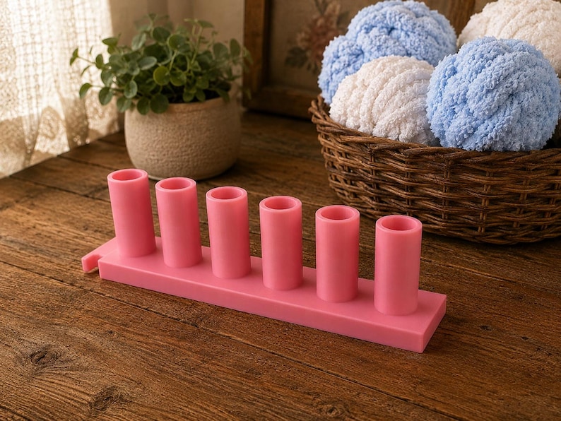 May include: A pink plastic organizer stand featuring six vertical cylindrical holders arranged in a single row on a rectangular base. The object is smooth, solid in color, and designed with a small tab extension on one side of the base structure.