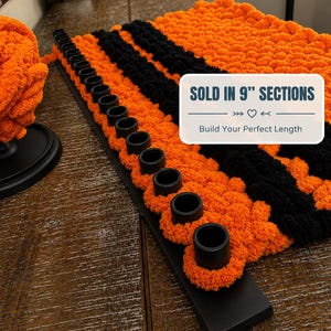 May include: A black rectangular base featuring a row of upright black cylindrical pegs, with thick orange and black yarn loops woven through the pegs. A white rectangular overlay displays the text SOLD IN 9" SECTIONS and Build Your Perfect Length.