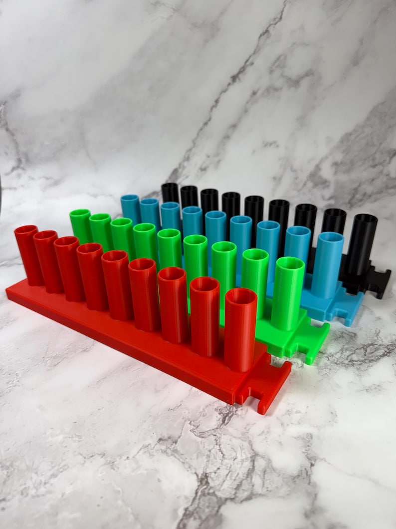 May include: A set of four rectangular storage racks, each featuring eight vertical cylindrical holders. The racks are colored red, green, blue, and black, arranged in a staggered formation. Each rack has a flat base with notched ends.