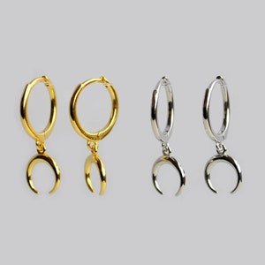 May include: A pair of gold and silver hoop earrings with crescent moon charms. The earrings are simple and elegant, perfect for everyday wear.