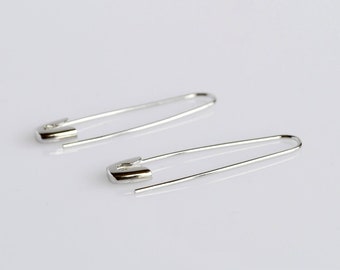 May include: A pair of silver safety pin earrings. The earrings are simple and minimalist, with a classic safety pin design.