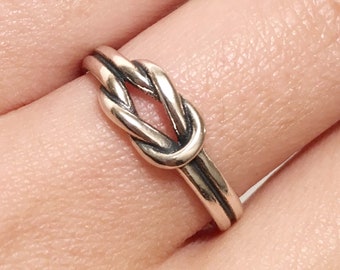 May include: A silver knot ring with a simple design. The ring is worn on a finger.