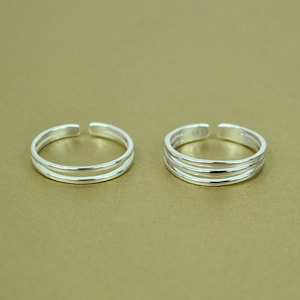 May include: Two silver toe rings with a double band design. The rings are simple and elegant.