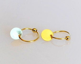 May include: A pair of gold hoop earrings with a small round disc charm. One earring has a white disc charm, and the other has a yellow disc charm.