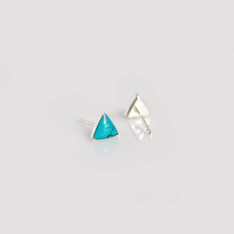 May include: A pair of silver triangle stud earrings with turquoise stones.