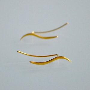May include: A pair of gold-toned earrings with a wavy design. The earrings are made of thin metal and have a delicate, minimalist look.