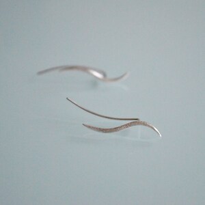 May include: A pair of silver earrings with a wavy design. The earrings are made of a thin, delicate wire and have a textured finish.