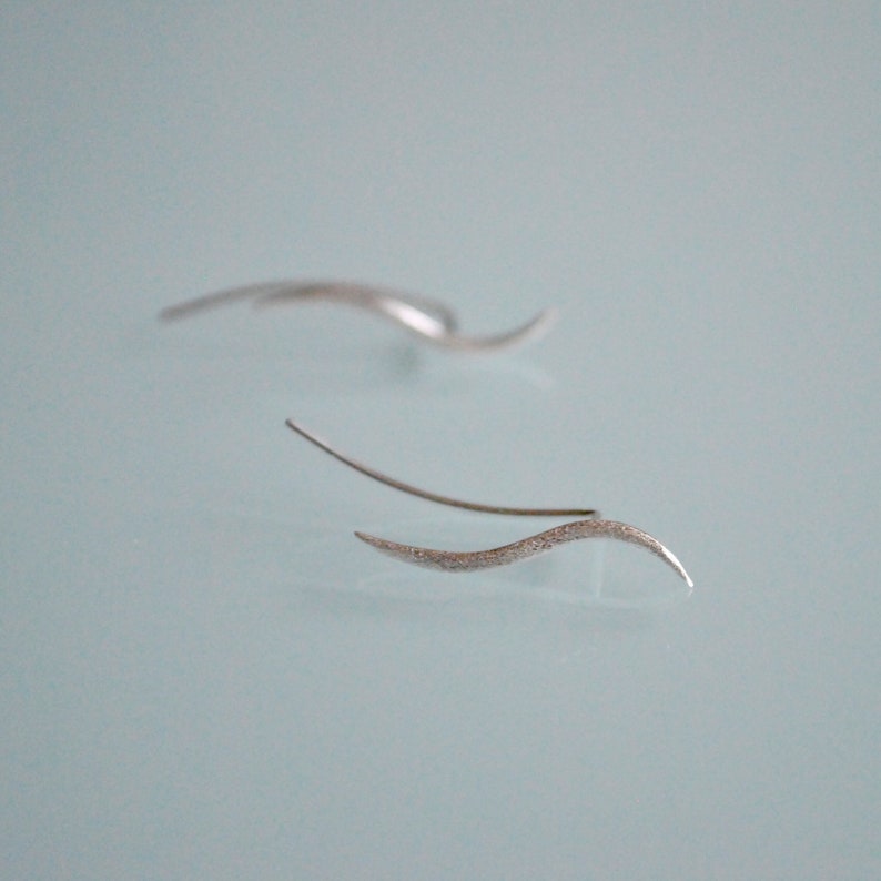 May include: A pair of silver earrings with a wavy design. The earrings are made of a thin, delicate wire and have a textured finish.
