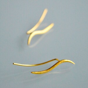 May include: A pair of gold-colored earrings with a wavy design. The earrings are made of thin metal and have a delicate, minimalist look.