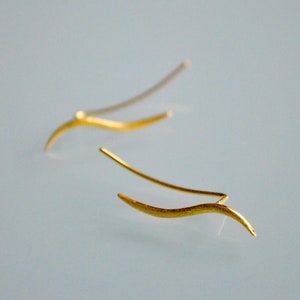 May include: A pair of gold-toned earrings with a curved, wavy design. The earrings are simple and elegant.