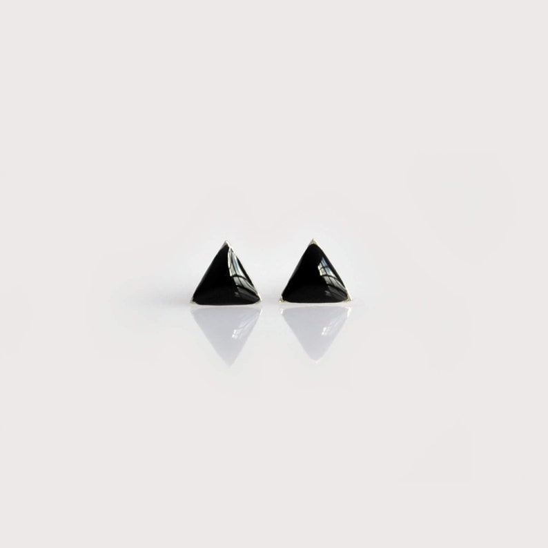 May include: A pair of black triangle-shaped stud earrings. The earrings are made of a shiny metal and have a simple, modern design.