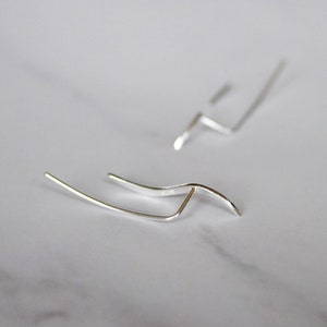 May include: A pair of silver earrings with a simple, modern design. Each earring features a curved, wave-like shape.