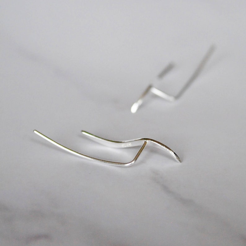 May include: A pair of silver earrings with a simple, modern design. Each earring features a curved, wave-like shape.