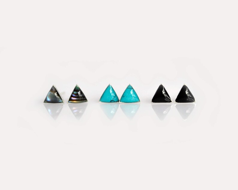 May include: A set of six triangle-shaped earrings with different colored stones. The earrings are made of silver and feature a turquoise, black, and iridescent abalone shell stones.