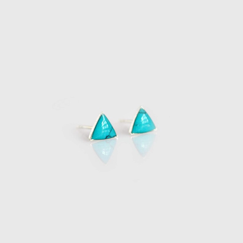 May include: A pair of silver triangle stud earrings with turquoise stones.