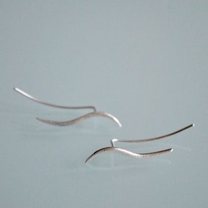 May include: A pair of silver ear cuffs with a wavy design. The cuffs are made of thin metal and have a brushed finish.