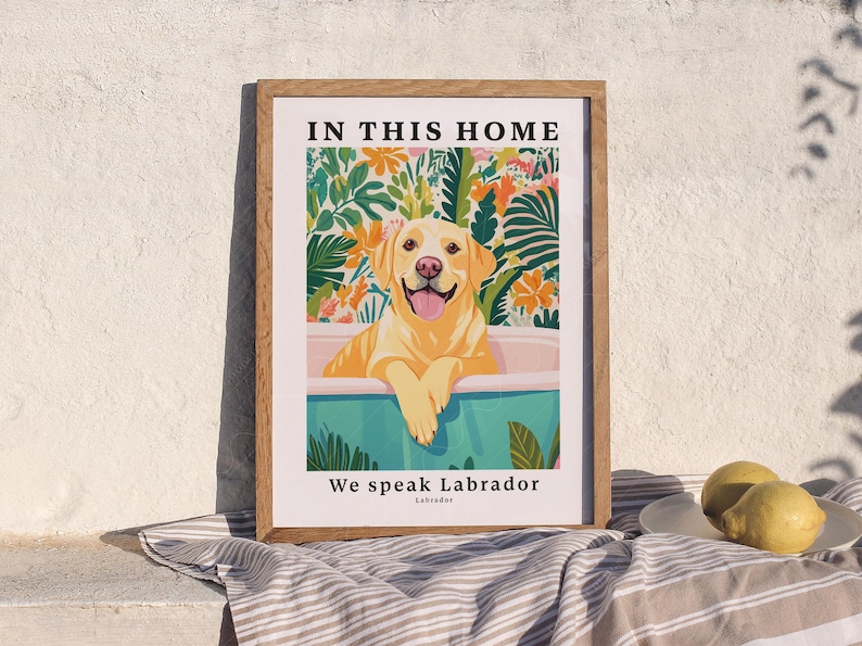 May include: A framed print with a yellow Labrador Retriever in a blue bathtub surrounded by tropical plants. The text "In this home we speak Labrador" is printed below the image.