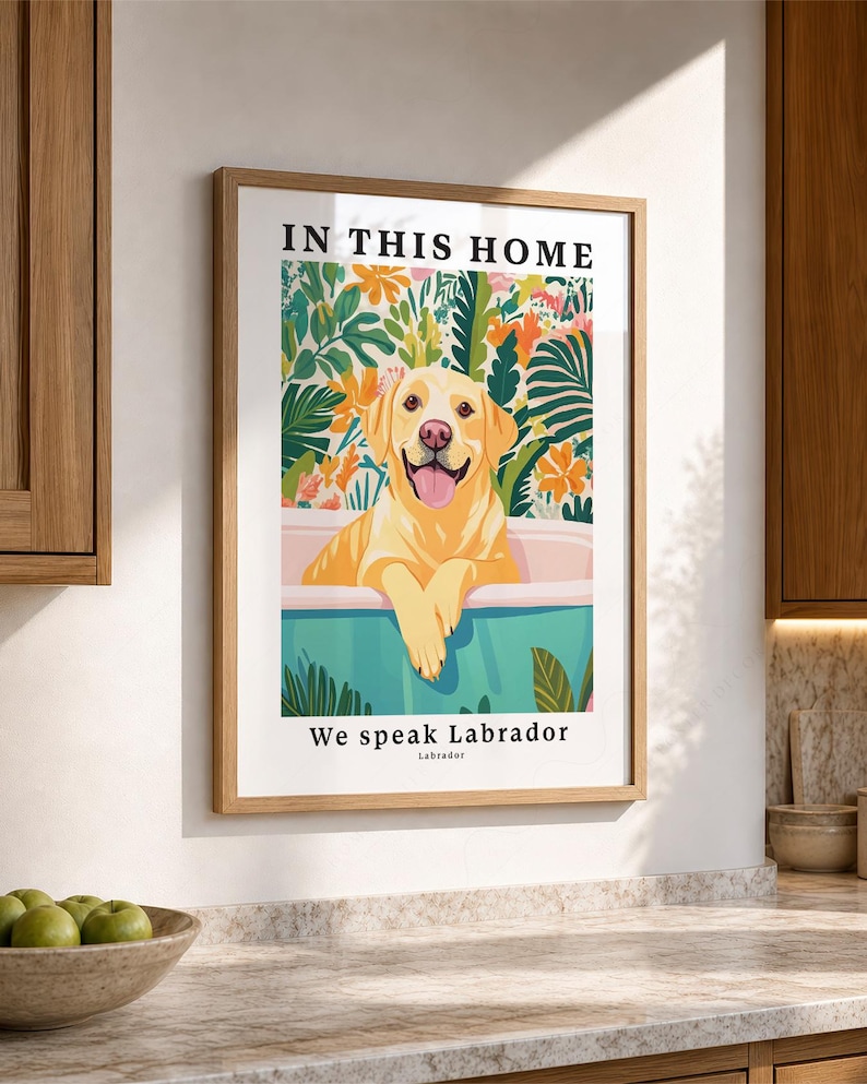 May include: A framed wall art print featuring a yellow Labrador retriever sitting in a light blue bathtub. The background displays colorful tropical leaves and flowers. The text reads IN THIS HOME at the top and We speak Labrador at the bottom.