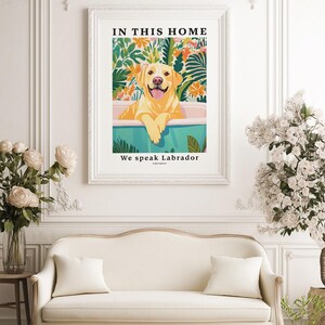 May include: A framed wall art print featuring a yellow Labrador retriever sitting in a teal bathtub. The background shows colorful tropical foliage and flowers. The text at the top reads IN THIS HOME and the bottom text reads We speak Labrador.