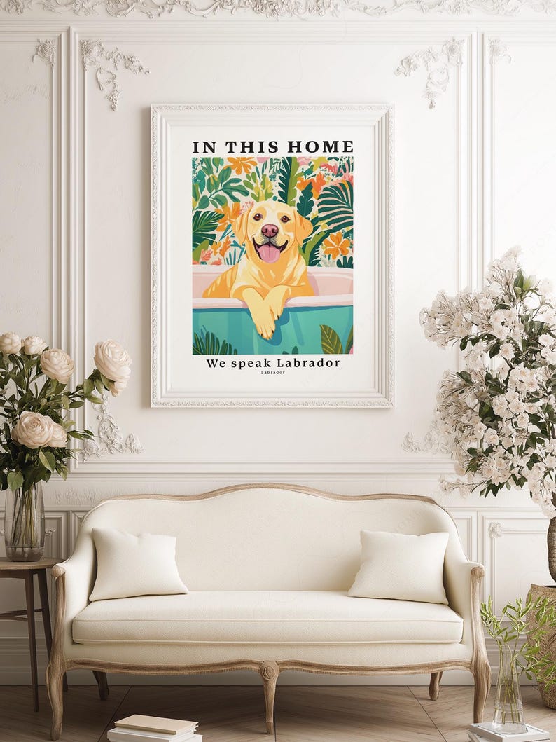 May include: A framed wall art print featuring a yellow Labrador retriever sitting in a teal bathtub. The background shows colorful tropical foliage and flowers. The text at the top reads IN THIS HOME and the bottom text reads We speak Labrador.