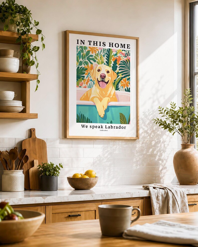 May include: A framed wall art print featuring a yellow Labrador retriever sitting in a bathtub surrounded by colorful tropical foliage. The text at the top reads IN THIS HOME and the text at the bottom reads We speak Labrador and Labrador.
