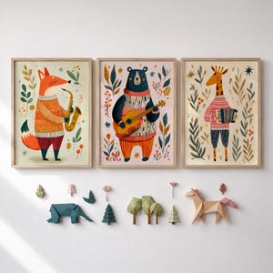 May include: Three framed wall art prints featuring a fox playing a saxophone, a bear playing a guitar, and a giraffe playing an accordion, all wearing sweaters. Below are small, geometric, paper-style wall decorations of an elephant, trees, and a horse.