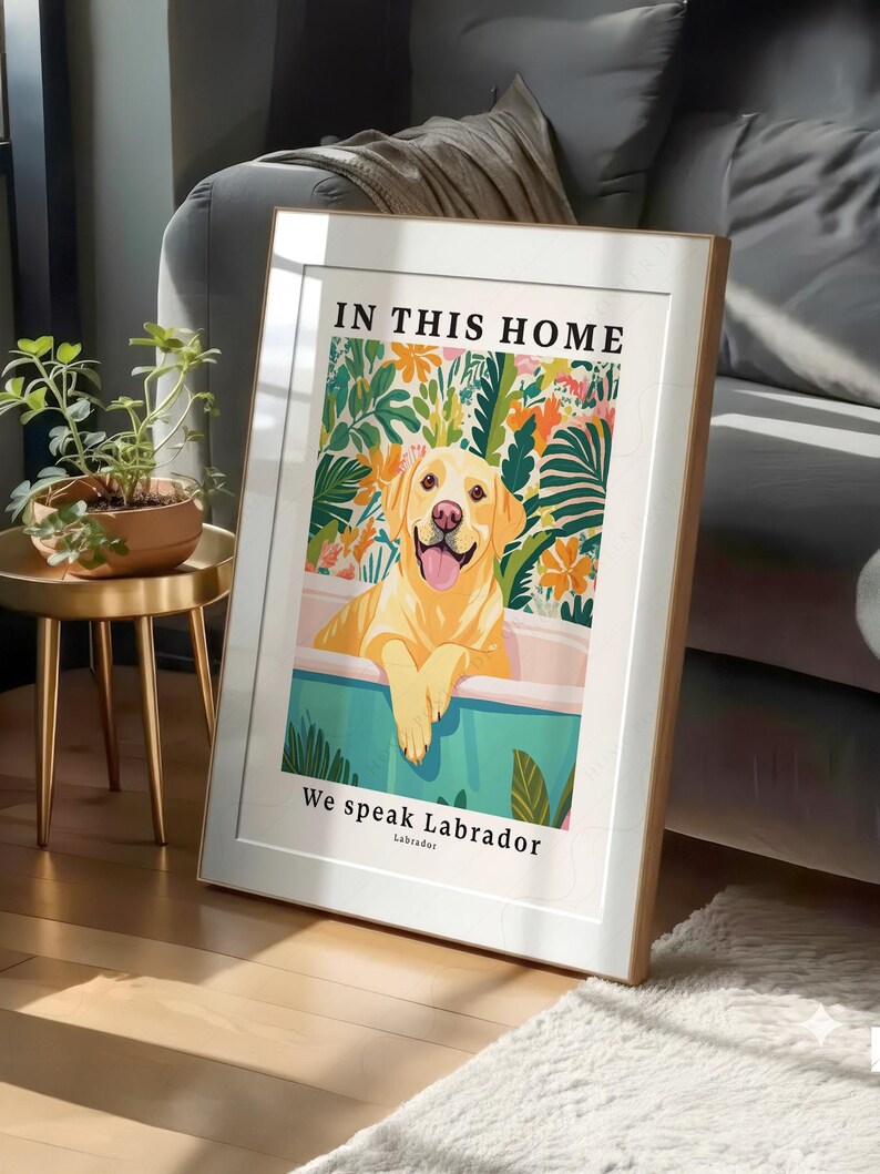 May include: A framed vertical wall art print featuring a yellow Labrador retriever sitting in a teal bathtub. The text reads IN THIS HOME at the top and We speak Labrador at the bottom. The background shows colorful tropical leaves and flowers.
