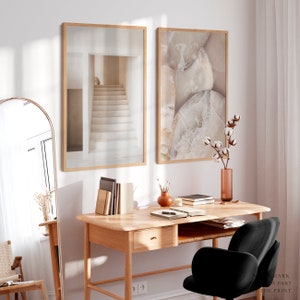 Puede incluir: Dos impresiones art&iacute;sticas enmarcadas. Una presenta una escalera en tonos neutros, la otra un primer plano de una formaci&oacute;n rocosa. Las impresiones cuelgan sobre un escritorio de madera con una silla negra, un espejo y objetos decorativos.