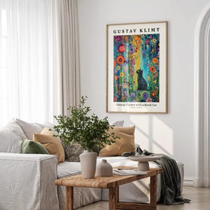 Pu&ograve; includere: Una stampa artistica incorniciata di "Cottage Garden with a Black Cat" di Gustav Klimt &egrave; appesa sopra un divano bianco. L'opera presenta una colorata scena floreale con un gatto nero. La stanza ha tende bianche e un tavolino di legno.