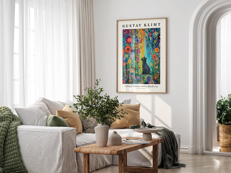 Pu&ograve; includere: Una stampa artistica incorniciata di "Cottage Garden with a Black Cat" di Gustav Klimt &egrave; appesa sopra un divano bianco. L'opera presenta una colorata scena floreale con un gatto nero. La stanza ha tende bianche e un tavolino di legno.