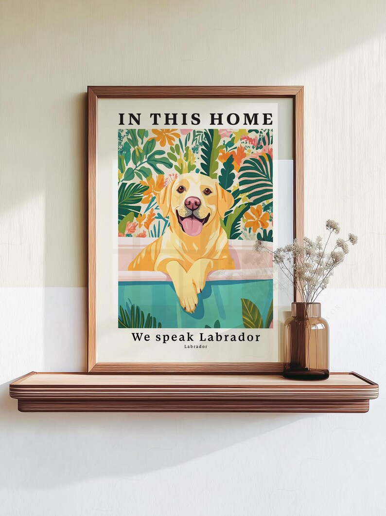 May include: A framed wall art print featuring a yellow Labrador retriever resting in a teal bathtub. The background displays colorful tropical foliage and flowers. The text reads IN THIS HOME at the top and We speak Labrador at the bottom.