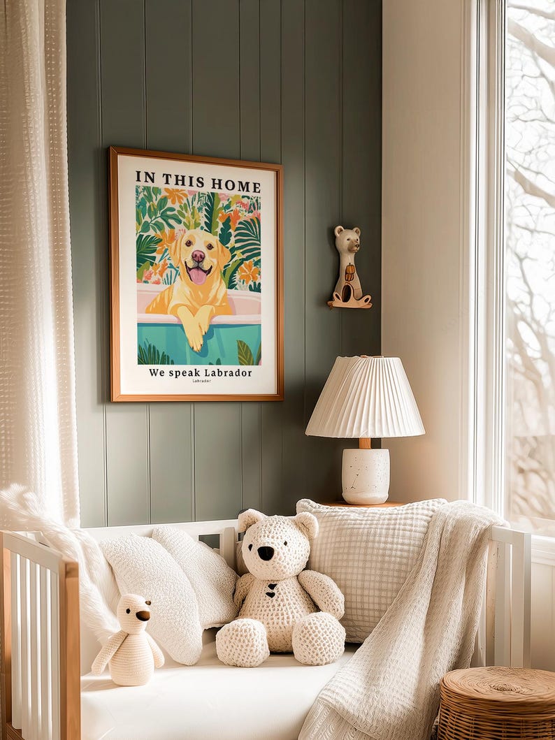 May include: A framed wall art print featuring a yellow Labrador retriever in a bathtub surrounded by colorful tropical foliage. The text reads IN THIS HOME at the top and We speak Labrador at the bottom. The print is displayed in a wooden frame.