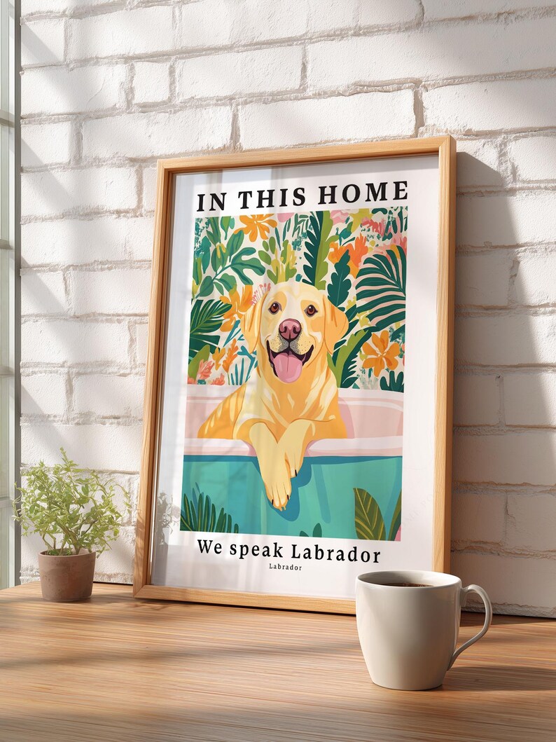 May include: A framed wall art print featuring a yellow Labrador retriever sitting in a bathtub. The illustration includes colorful tropical foliage in the background and the text "IN THIS HOME" at the top and "We speak Labrador" at the bottom.