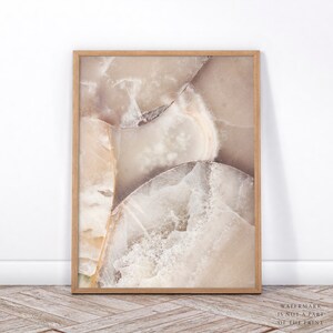 Puede incluir: Una impresi&oacute;n enmarcada que presenta un primer plano de una piedra pulida con un dise&ntilde;o natural y abstracto. La obra de arte muestra una mezcla de tonos beige, crema y marr&oacute;n claro, con vetas y estructuras cristalinas visibles. El marco de madera a&ntilde;ade calidez.