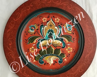 May include: A round, red wooden plate with a teal border and a hand-painted floral design in shades of red, yellow, green, and blue.