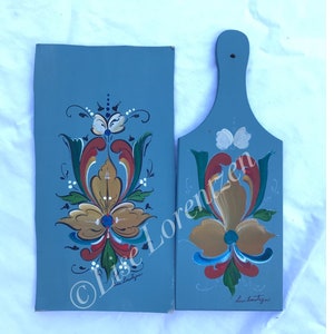 Puede incluir: Dos tablas de cortar de madera pintadas de azul con un diseño floral en rojo, amarillo, verde y blanco. Las tablas están firmadas "Lise Lorenzen".