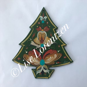 May include: A wooden Christmas tree ornament with a green background and gold trim. The tree is decorated with floral designs in shades of orange, yellow, and white, with turquoise accents. The artist's signature is visible.