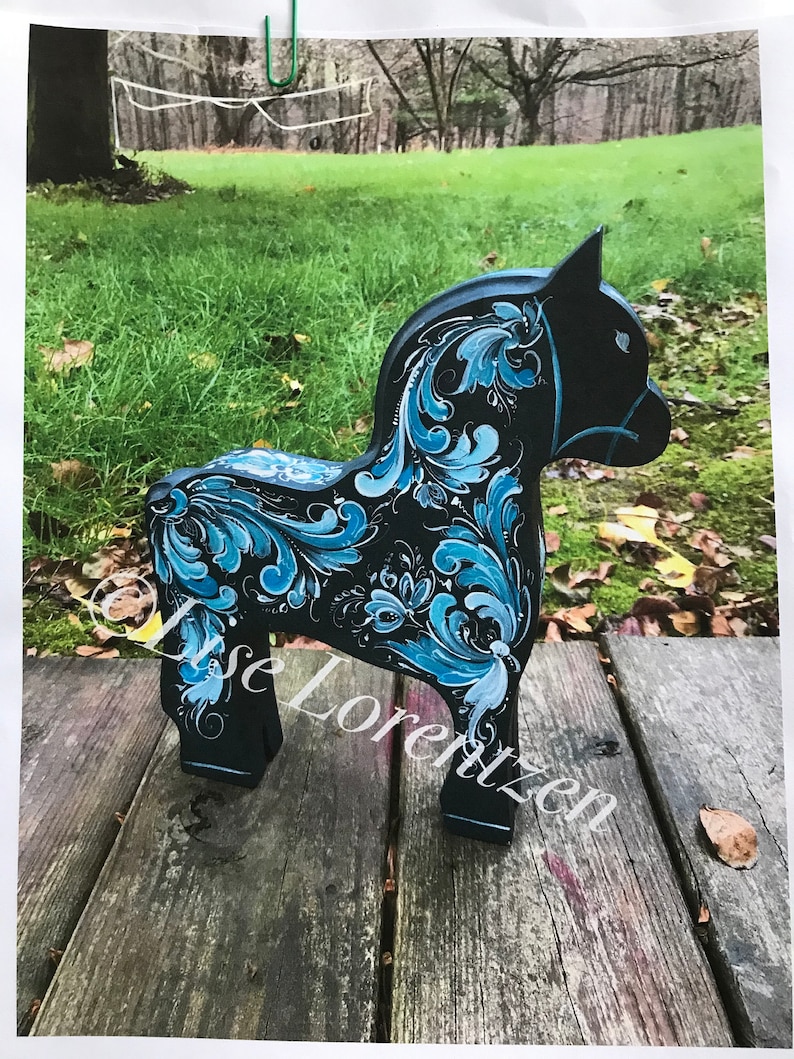 May include: A hand-painted wooden horse with blue and black floral designs. The horse is standing on a wooden surface.