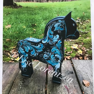 May include: A hand-painted wooden horse with blue and black floral designs. The horse is standing on a wooden surface.