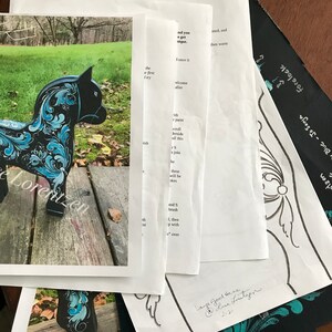 May include: A black wooden horse with blue and white painted floral designs. The horse is standing on a wooden surface. The image also includes a close-up of the horse's head and a sheet of paper with instructions for painting.