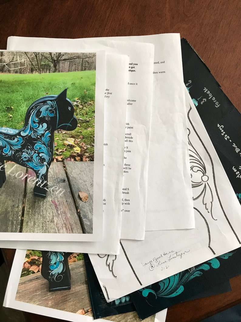 May include: A black wooden horse with blue and white painted floral designs. The horse is standing on a wooden surface. The image also includes a close-up of the horse's head and a sheet of paper with instructions for painting.