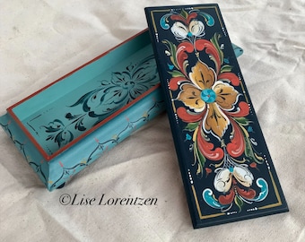May include: A hand-painted wooden box with a teal blue lid and a black base. The lid features a floral design in shades of teal, red, and gold. The base features a similar floral design in shades of red, gold, and white. The box is signed "Lise Lorentzen".